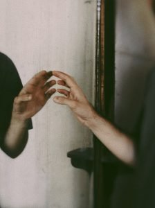 A persons hand reaching towards its reflection in a mirror, creating a mysterious mood.