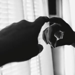 A dramatic black and white photo of a hand reaching toward a mirror, creating a reflective illusion.